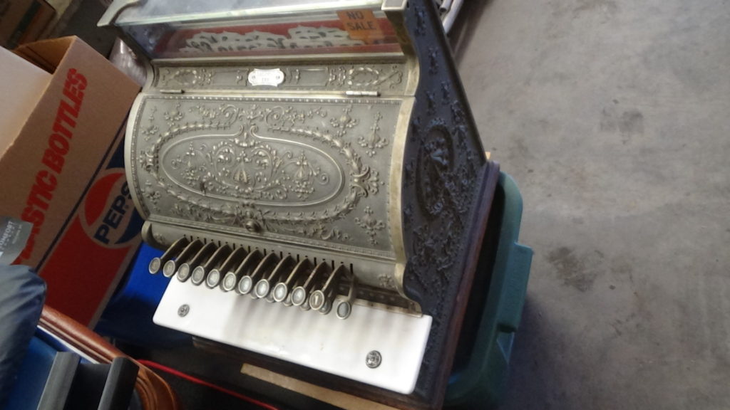 An old cash register stacked on top of a gray container. 
