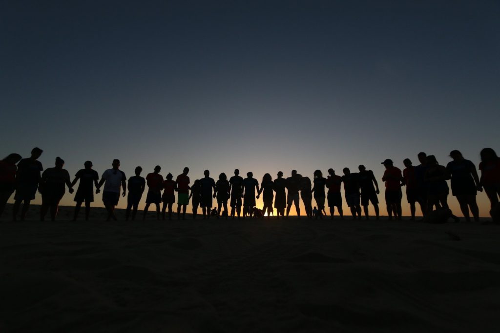 Long line of people standing side-by-side silhouetted against an early morning sky